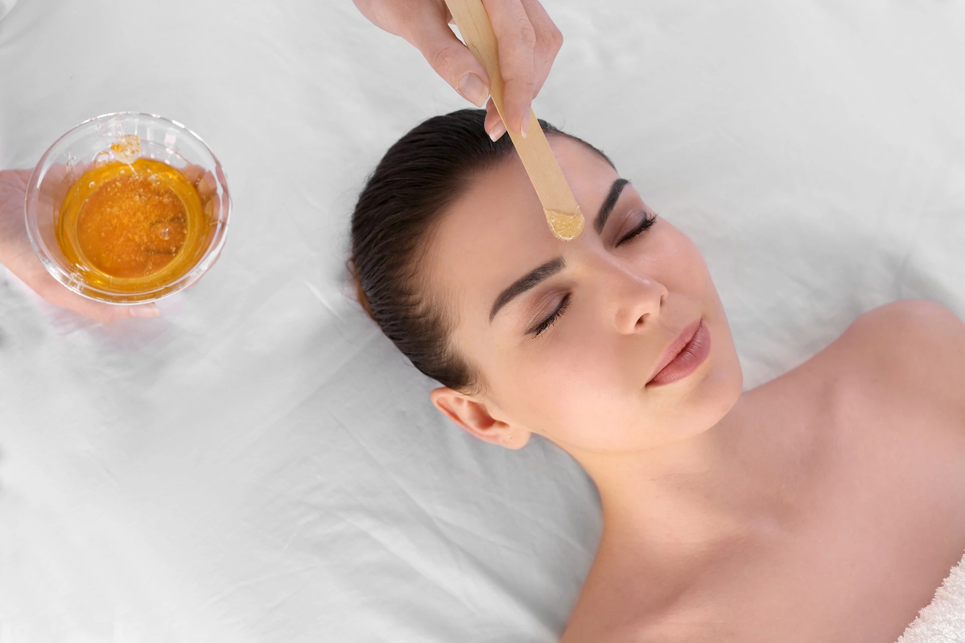 a woman lying down with a wax stick on her forehead